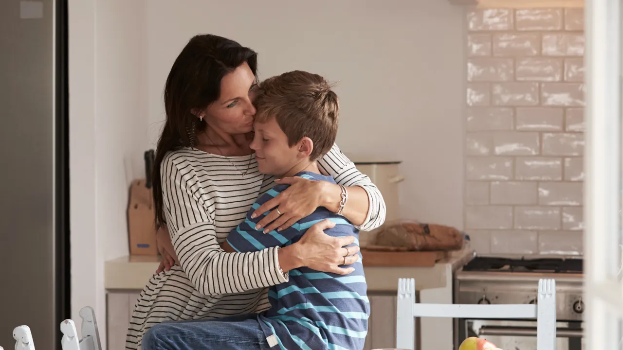 Mor og sønn gir hverandre en klem på kjøkken.