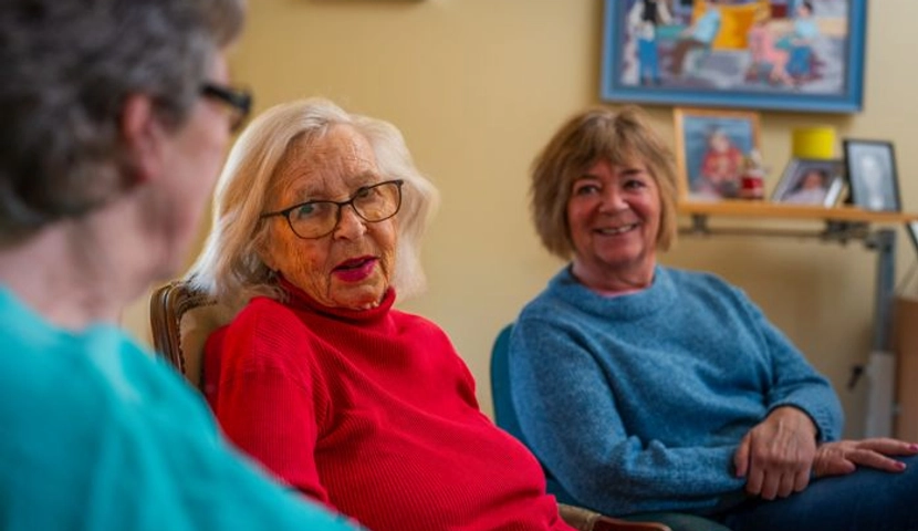 En kvinne i rød genser sitter ved siden av en kvinne i blå genser.