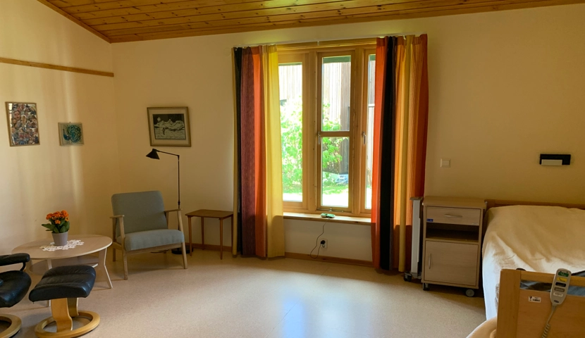 Et rom med en seng, en stol, et bord og et vindu.