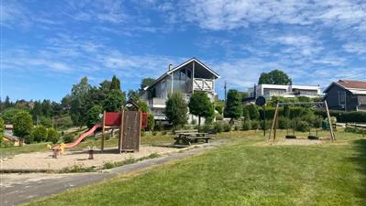 En park med en lekeplass og hus i bakgrunnen.