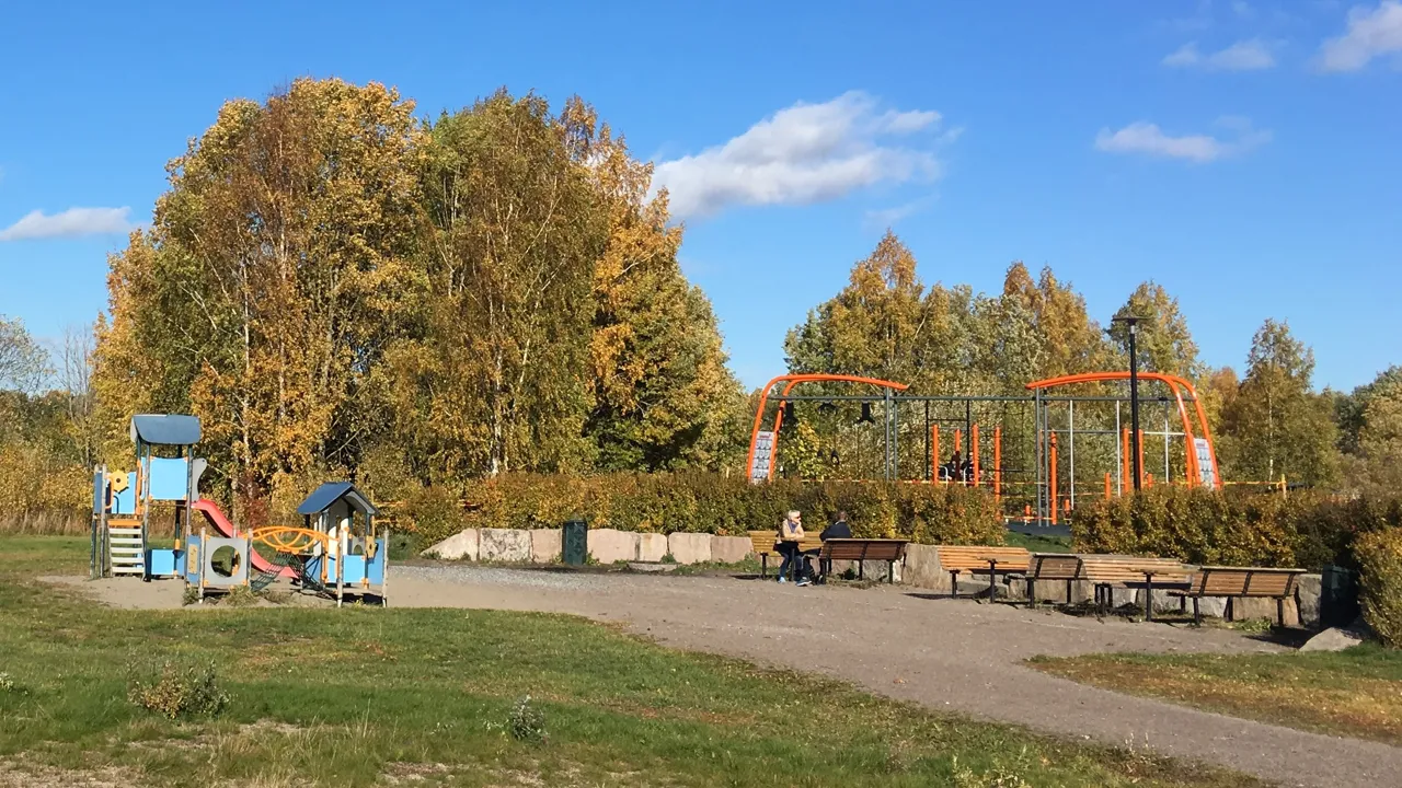 En park med lekestruktur og piknikbord.