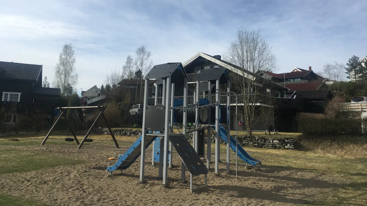 En lekeplass med en blå sklie og et hus i bakgrunnen.