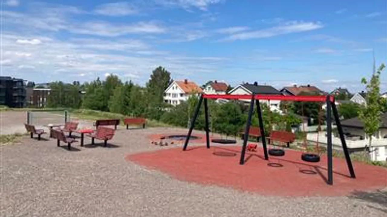 En lekeplass med husker og benker i en park.