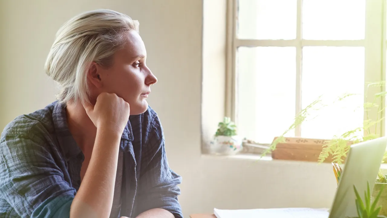 En dame som sitter ved en pult og ser ut av vinduet.