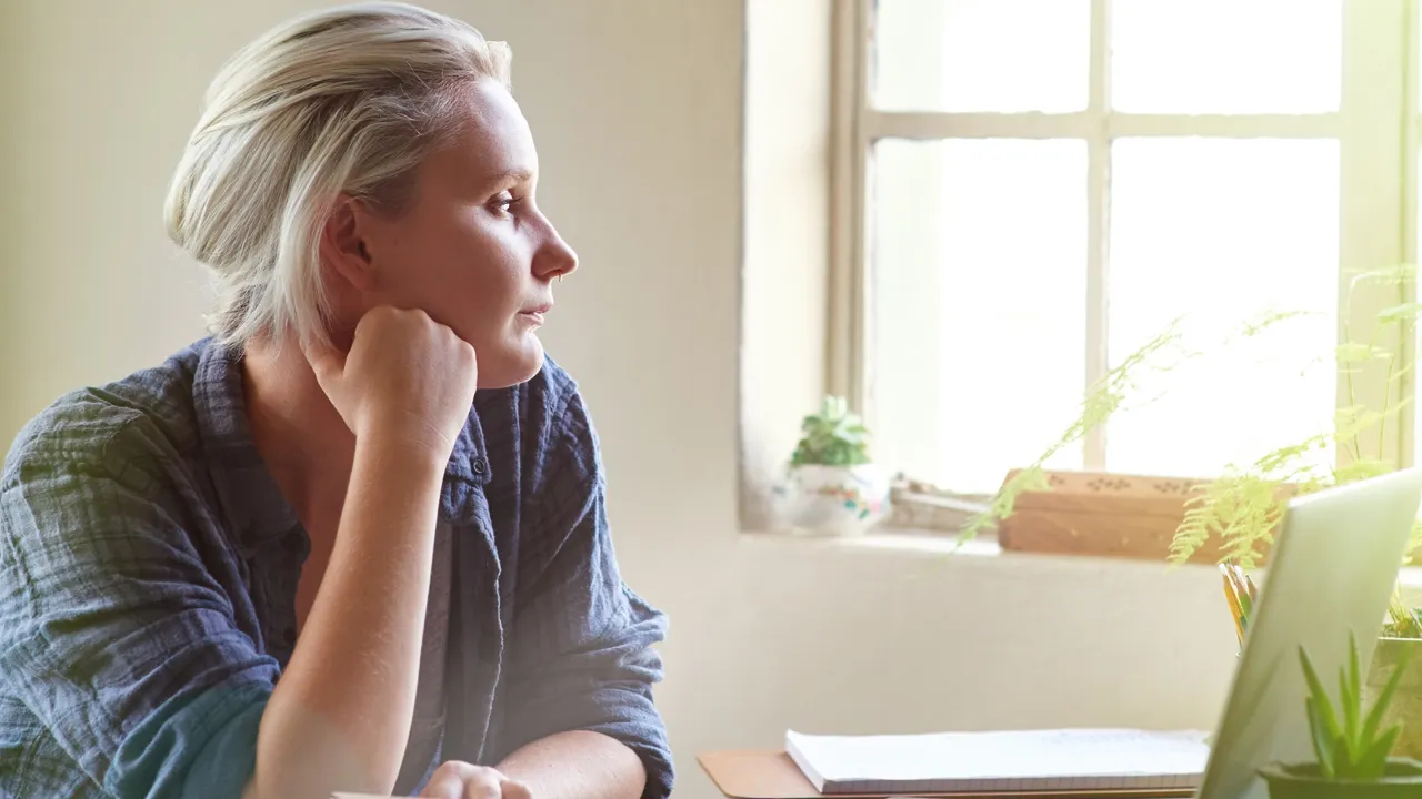 En dame som sitter ved en pult og ser ut av vinduet.