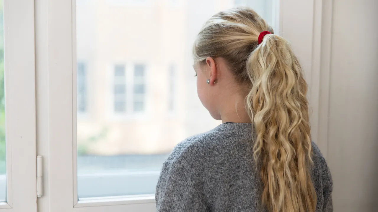 En jente med hestehale som ser ut av et vindu.