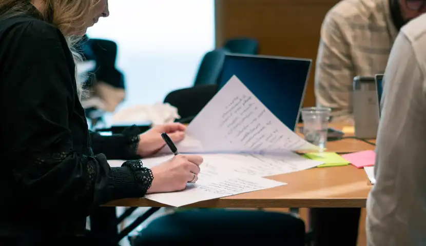 En kvinne sitter ved et bord og skriver p&aring; et stykke papir.