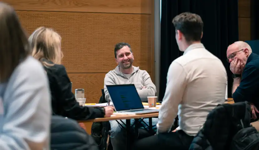 En gruppe mennesker som sitter rundt et bord med en b&aelig;rbar datamaskin.