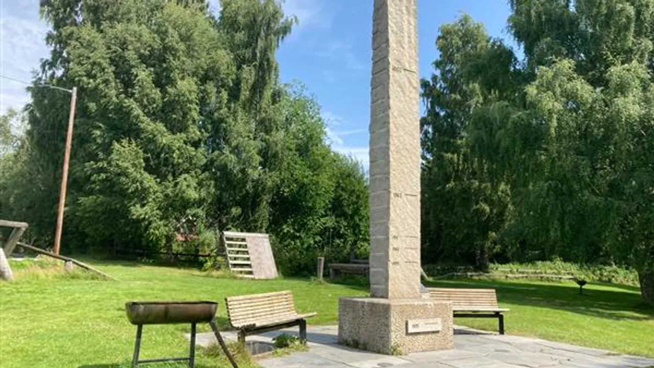 Et monument midt i en park med en grill ved siden av.