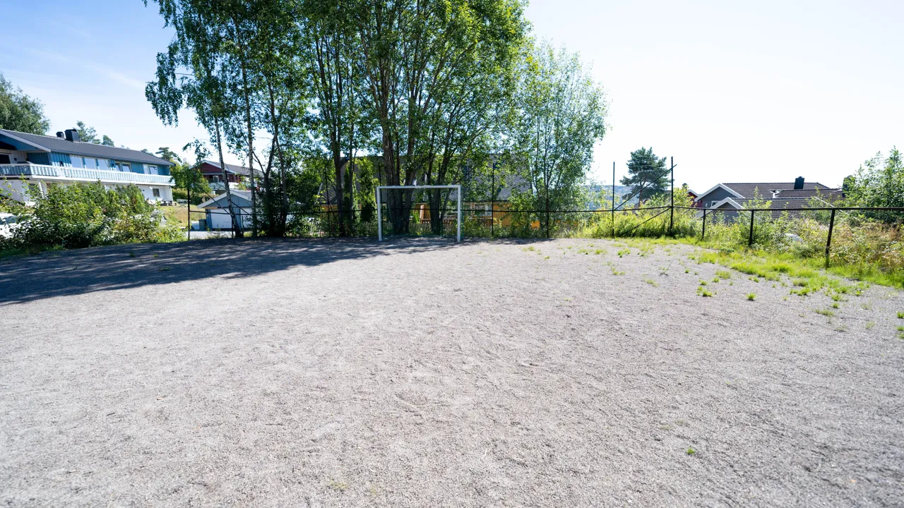 En grusbane med et gjerde og trær i bakgrunnen.