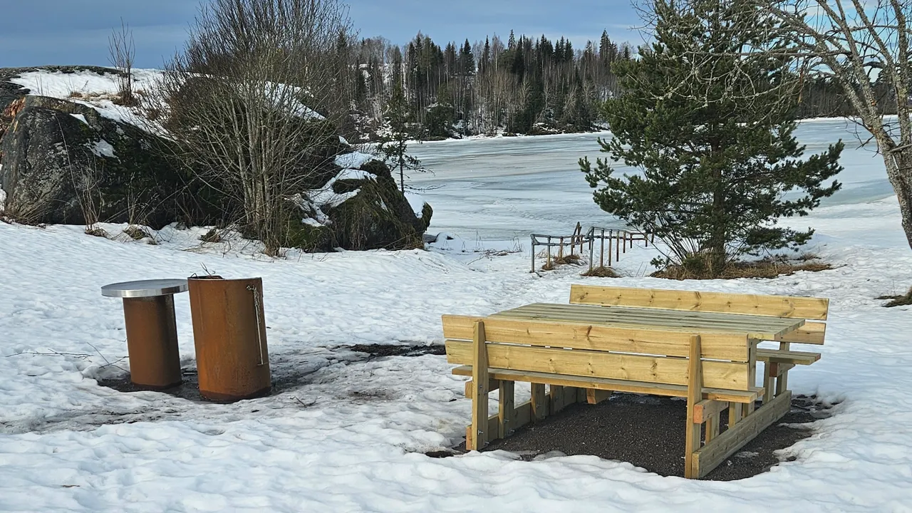 En trebenk og en grillplass ved et vann.