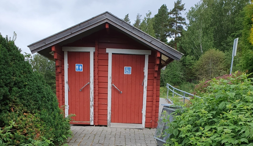 En liten rød bygning med to toaletter.