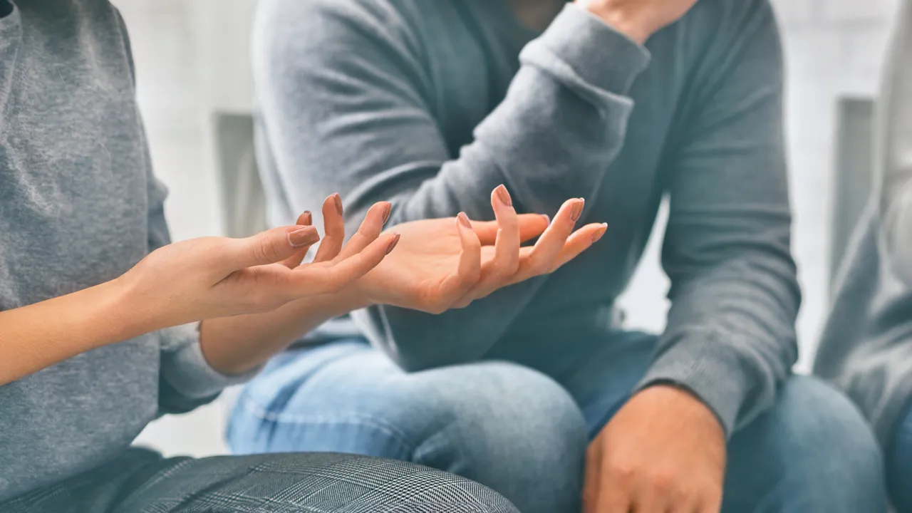 En gruppe mennesker som sitter i en sirkel med hendene samlet.