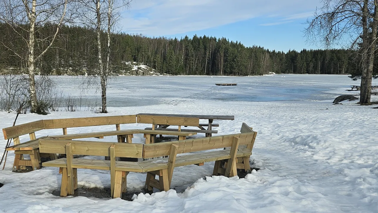 Trebenker med en bålplass i midten ved et vann.