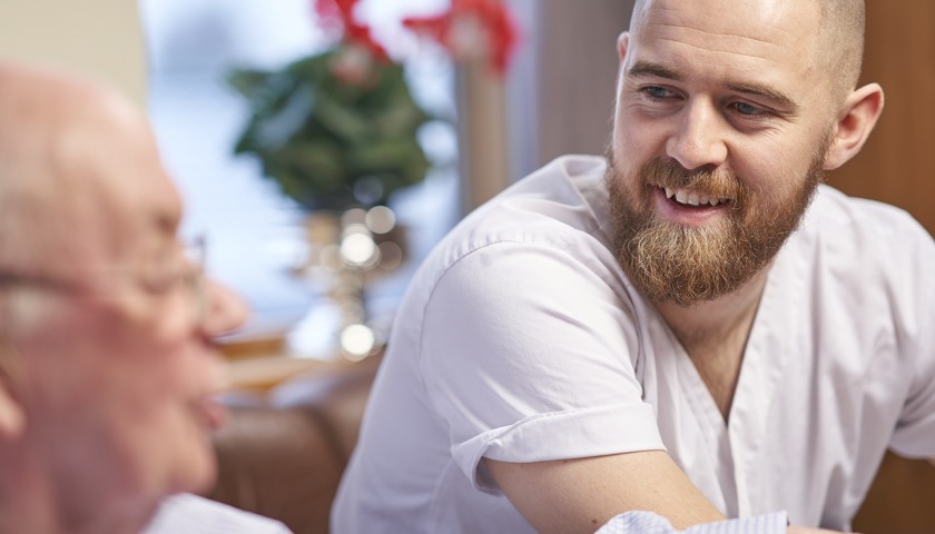 Mann i sykepleieruniform som smiler