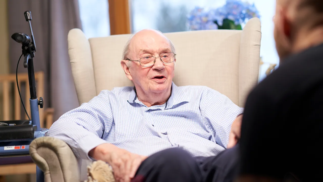 Gammel mann sitter i stol og snakker