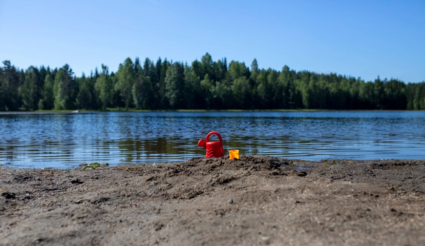 En rød bøtte og en gul spade i sanden.