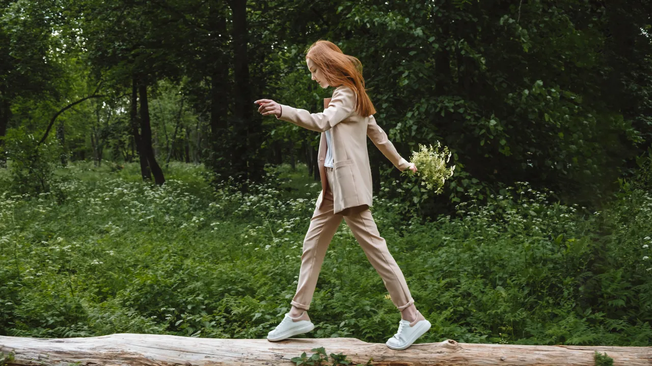 En ung jente som går over en tømmerstokk i en skog.