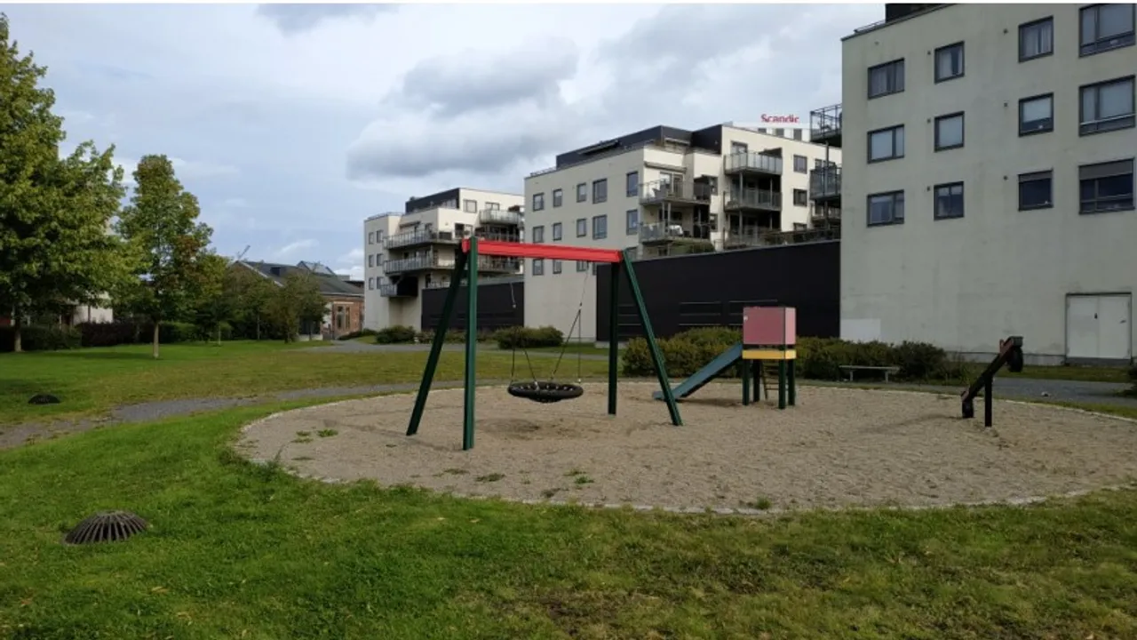 En lekeplass med huskestativ og en bygning i bakgrunnen.