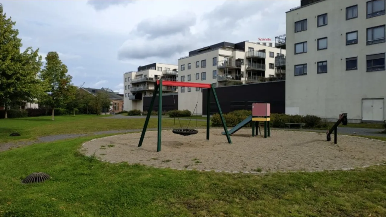 En lekeplass med huskestativ og en bygning i bakgrunnen.