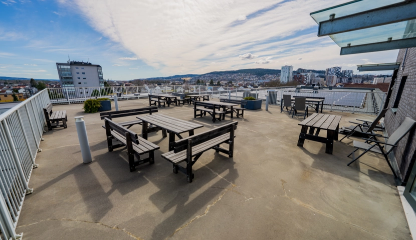 En takterasse med piknikkbord og utsikt over Lillestrøm.