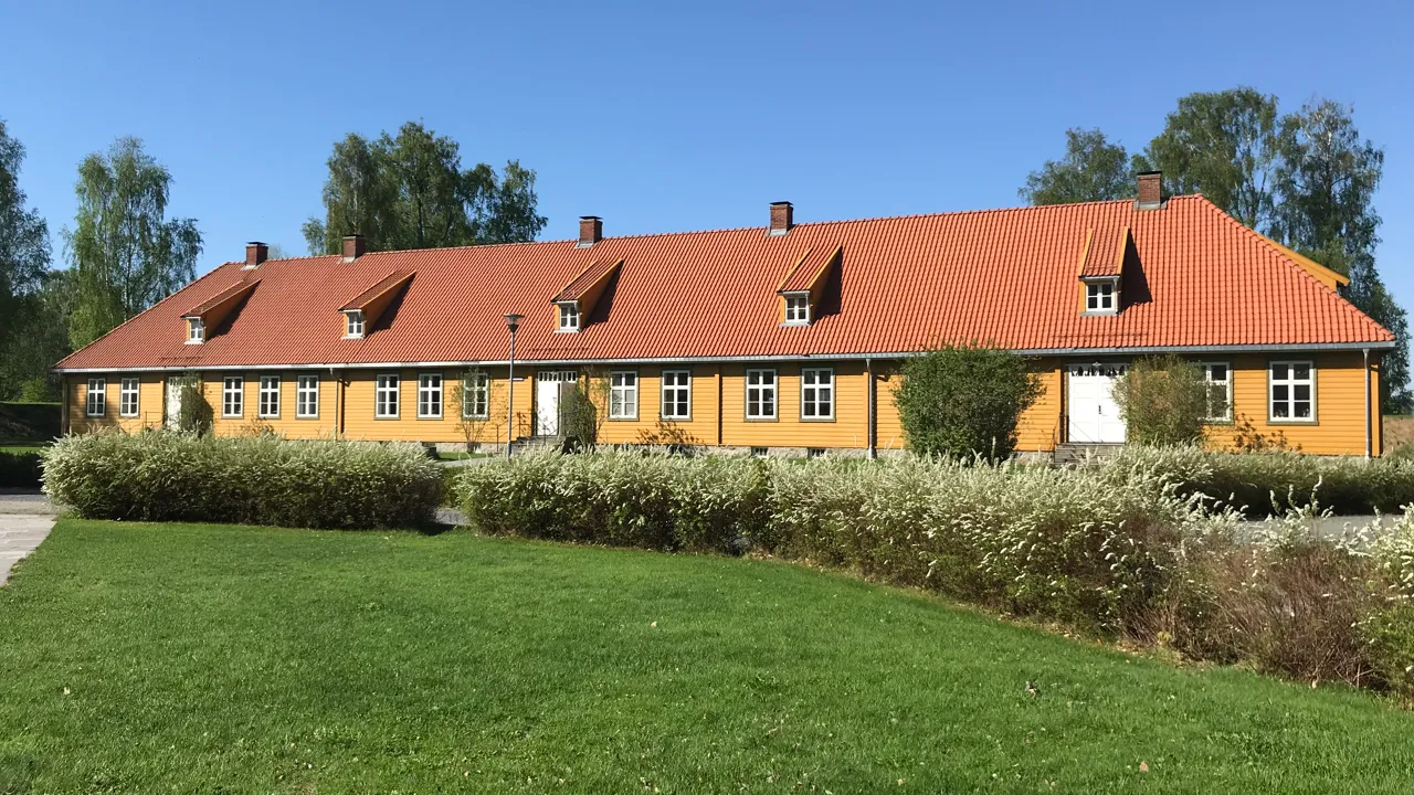 Kommandantboligen er et gult hus med rødt tak og noen busker.