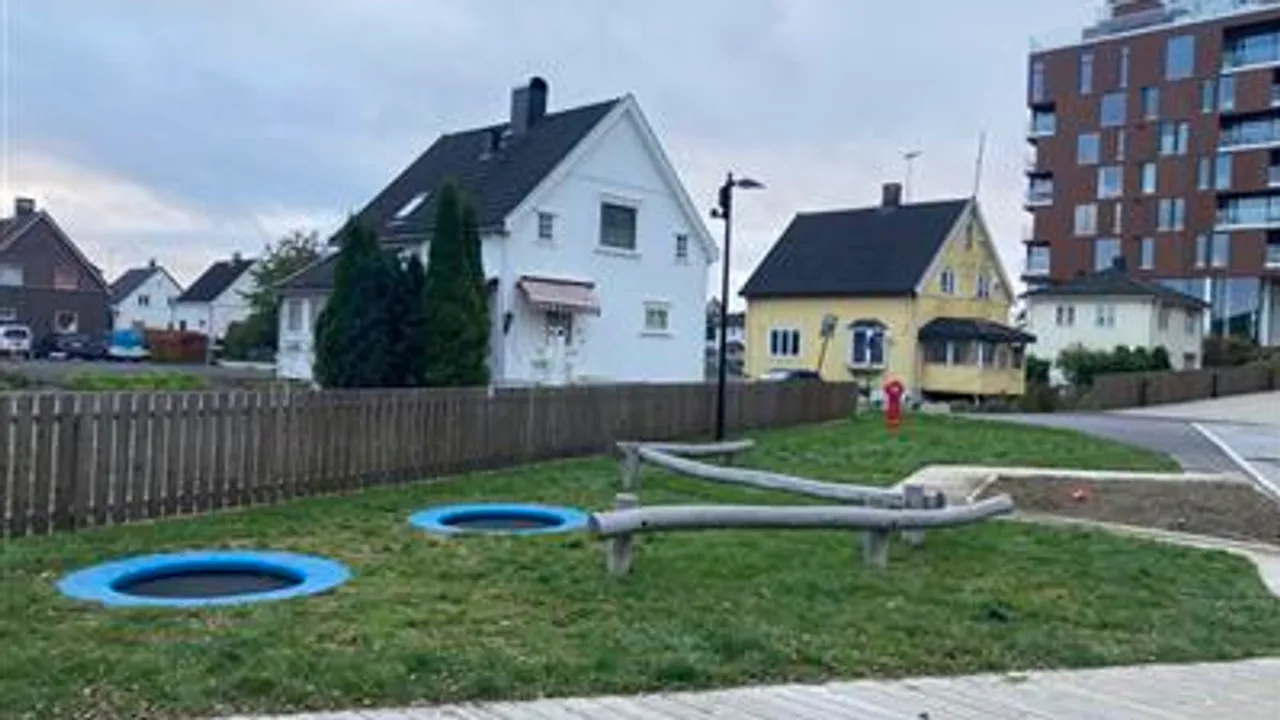 Et gressområde med lekeplass og et tregjerde.