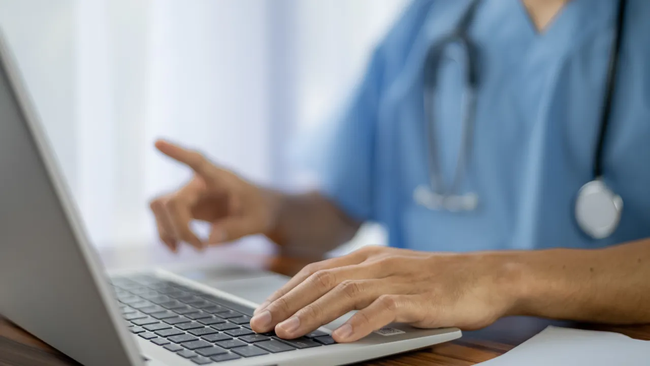 En lege som bruker en bærbar datamaskin på et skrivebord.