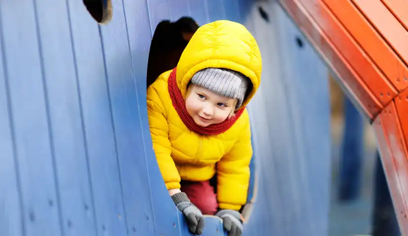 Barn titter frem fra fra liten bygning på lekeplass