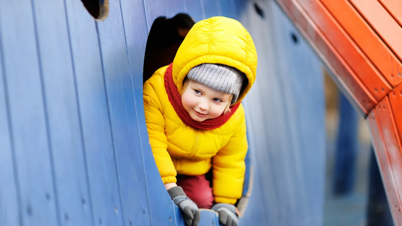 Barn titter frem fra fra liten bygning på lekeplass