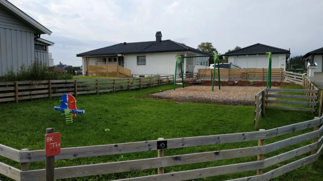 En inngjerdet hage med lekeplass og et lekeområde.