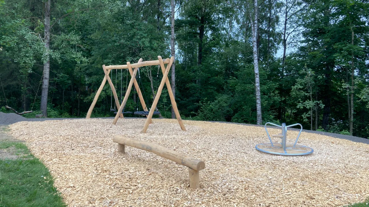 En huske av tre i en park ved siden av en skog.