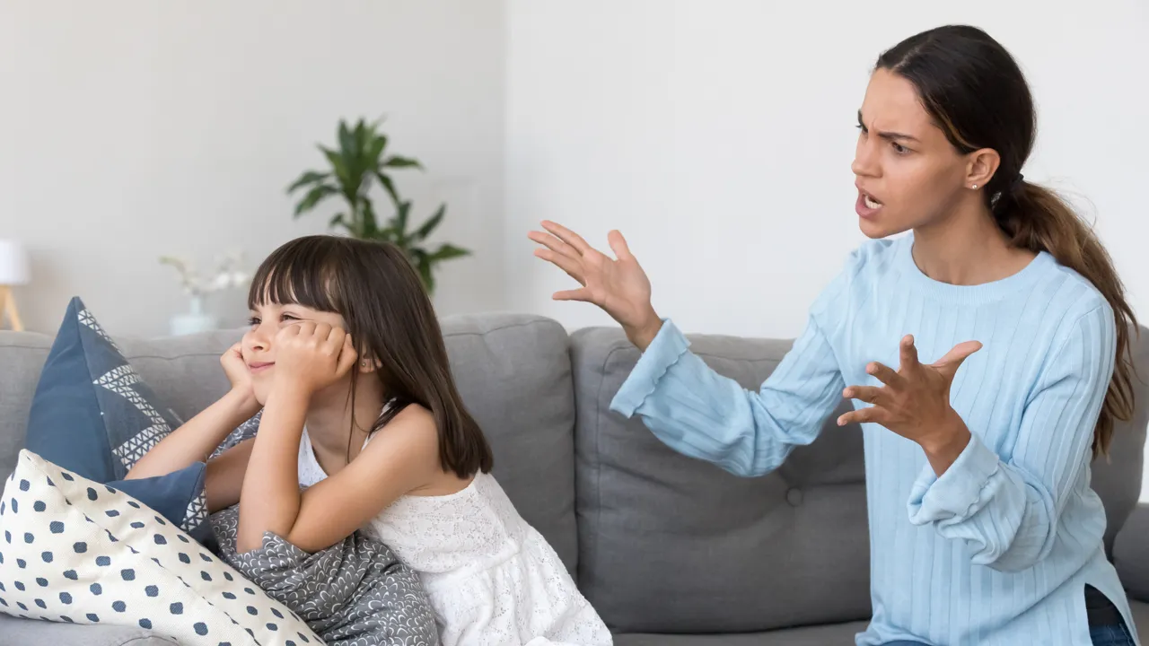 En kvinne sitter i en sofa og kjefter på en liten jente.