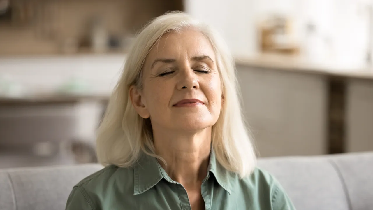 En kvinne sitter på en sofa med lukkede øyne.