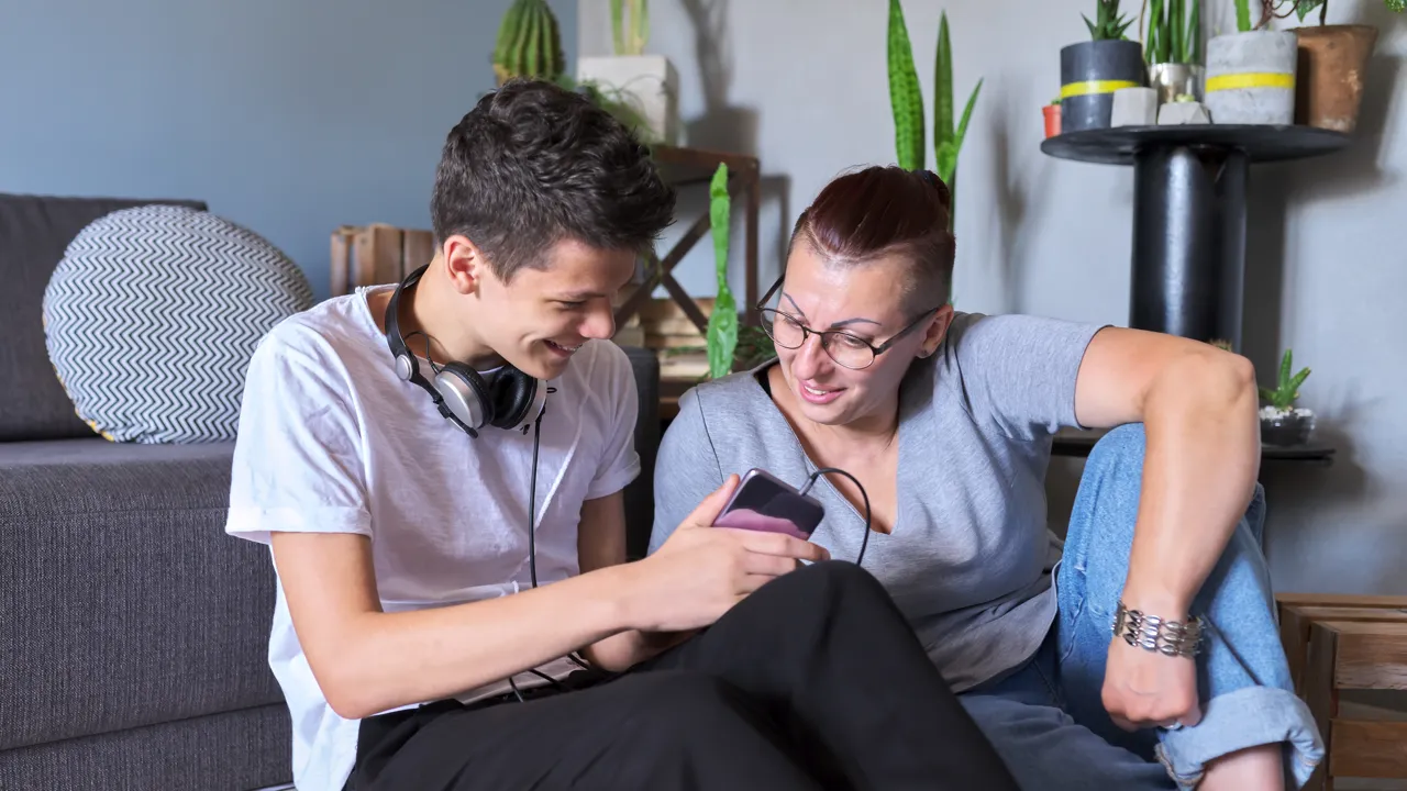 En mann og en kvinne sitter i en sofa og ser på en mobiltelefon.