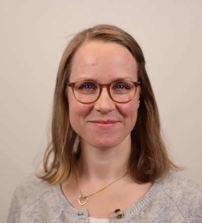 En kvinne med briller og grå genser.