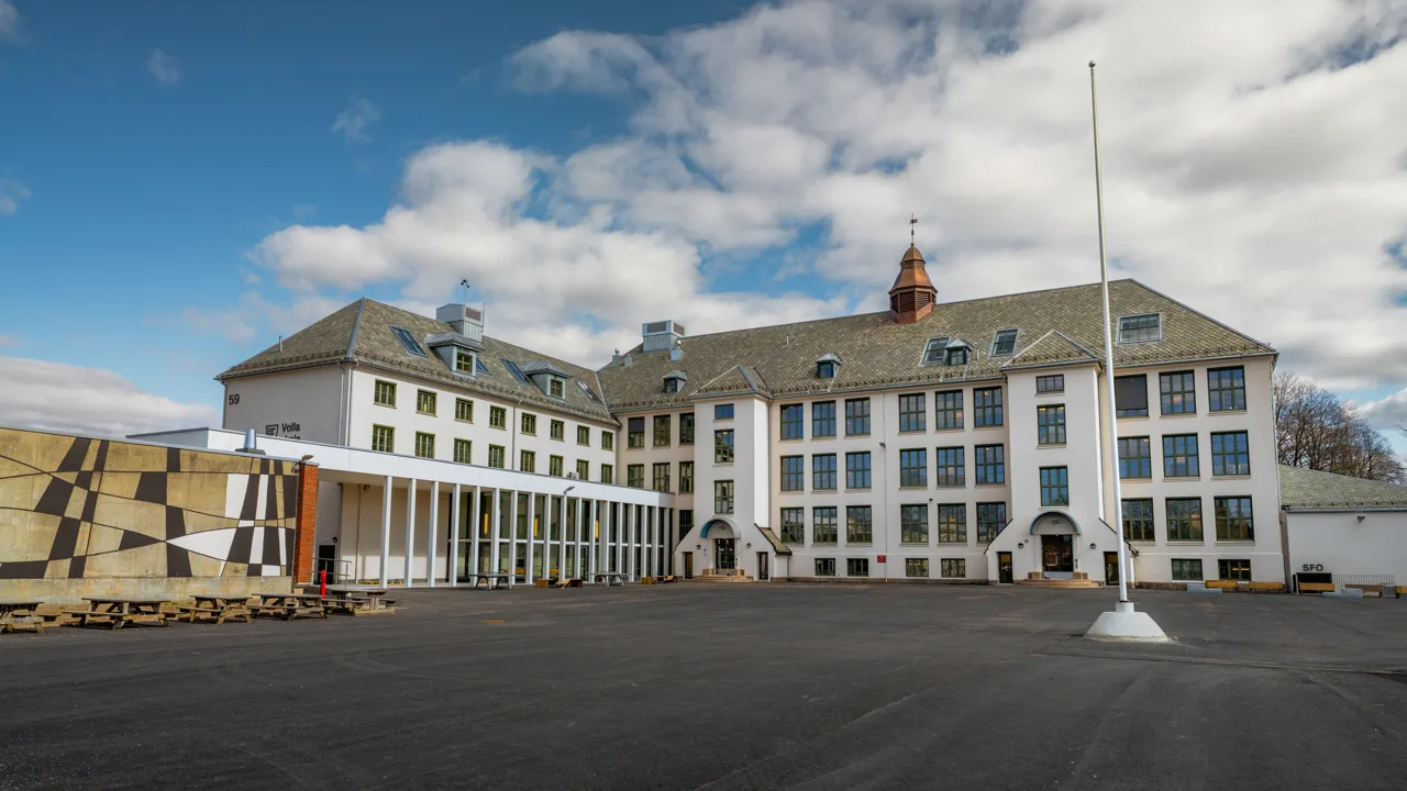 En stor hvit bygning med en stor plass og flaggstang foran.