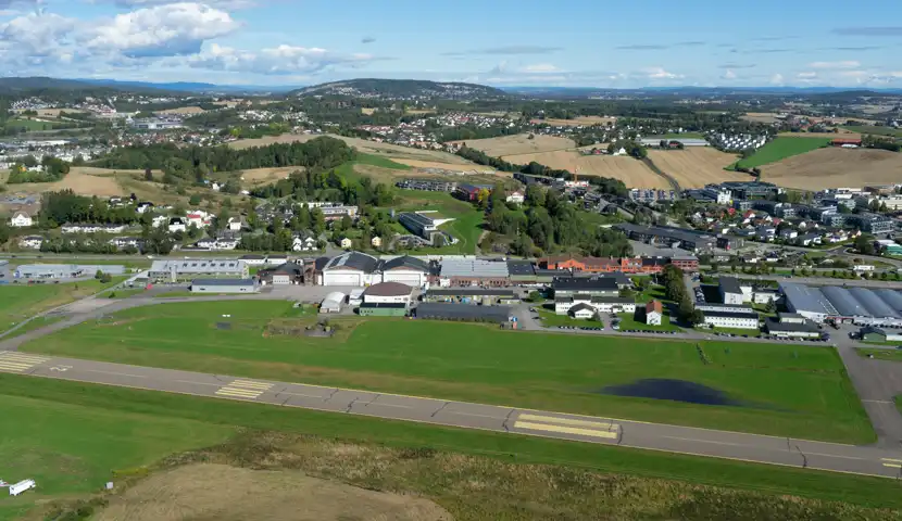 Luftfoto av rullebane på en liten flyplass med boligområde og landbruksområde i bakgrunnen