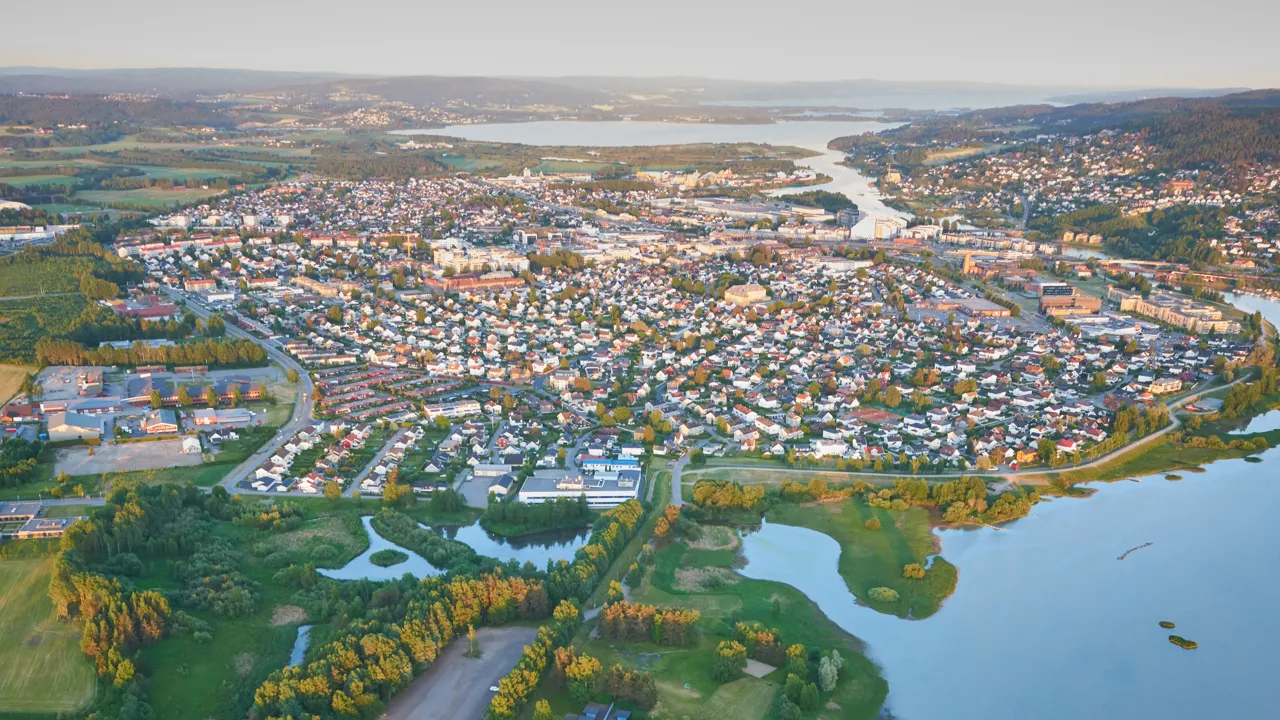 Et luftfoto av et område med mye bebyggelse og ei elv og et friluftsområde med utendørs basseng