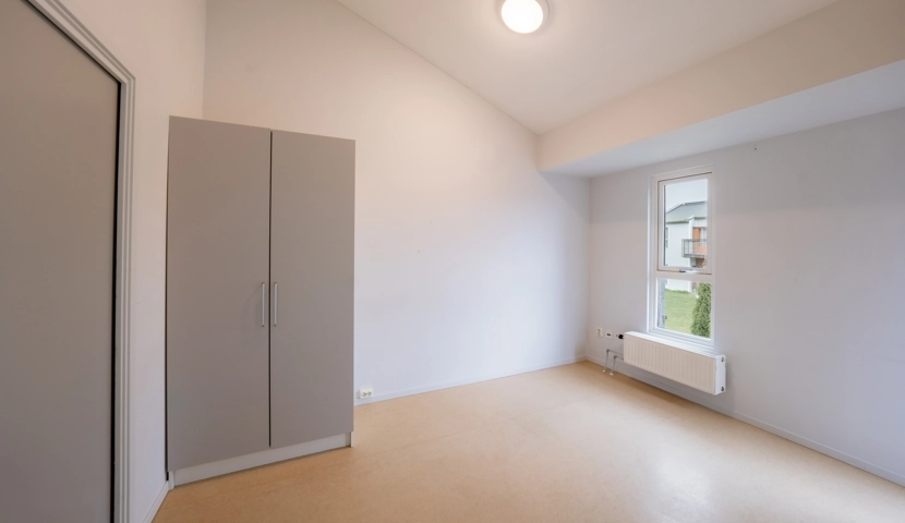 Et soverom med skap, vindu og en radiator.