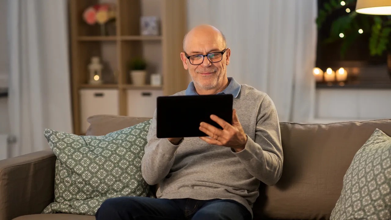 En mann som sitter på en sofa og holder et nettbrett.