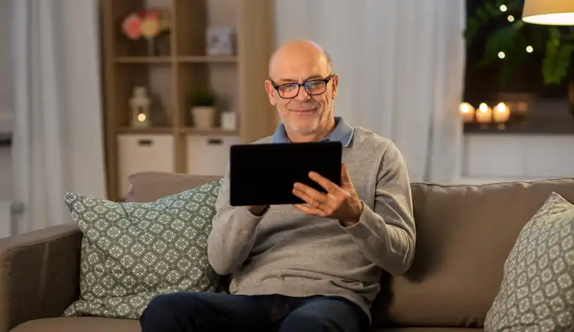 En mann som sitter på en sofa og holder et nettbrett.