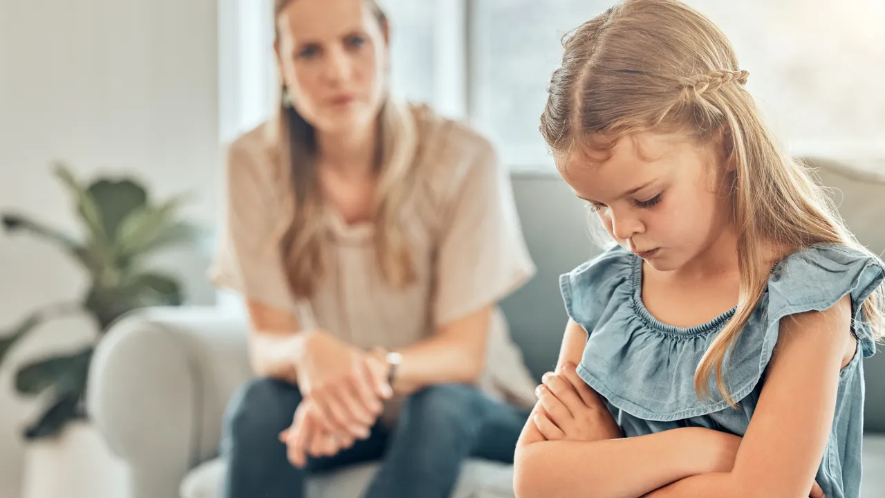 En kvinne sitter på en sofa ved siden av en liten jente som er sint.