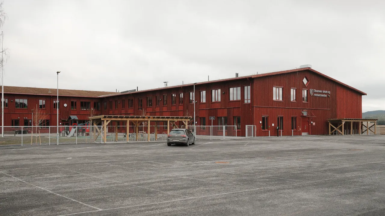 Et rødt skolebygg med en parkeringsplass foran