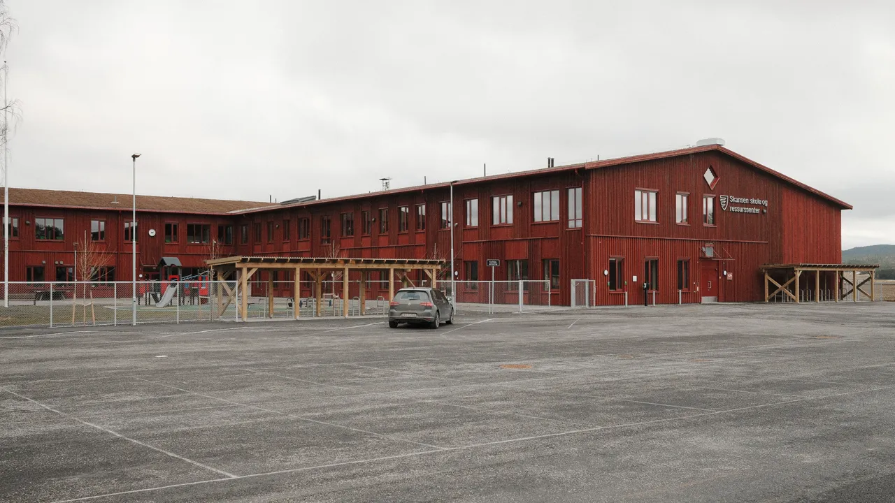Et rødt skolebygg med en parkeringsplass foran