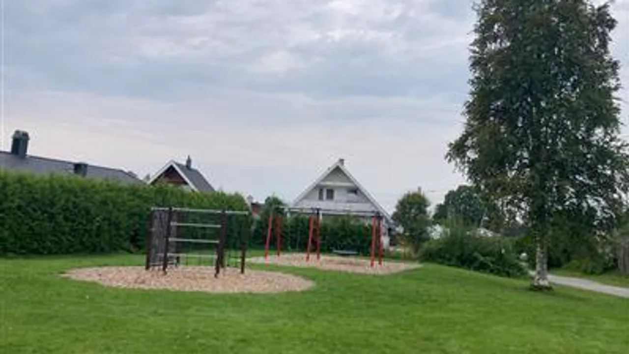 En park med en lekeplass og et hus i bakgrunnen.
