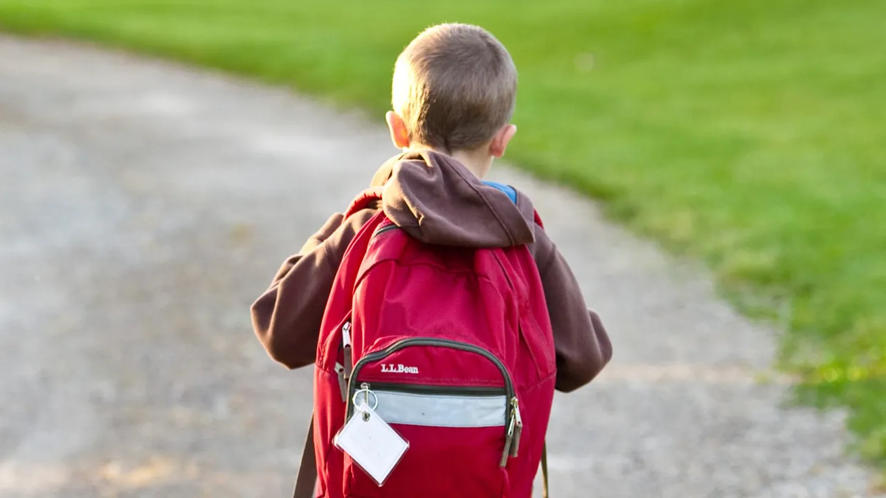 Liten gutt går bortover veien med skolesekk