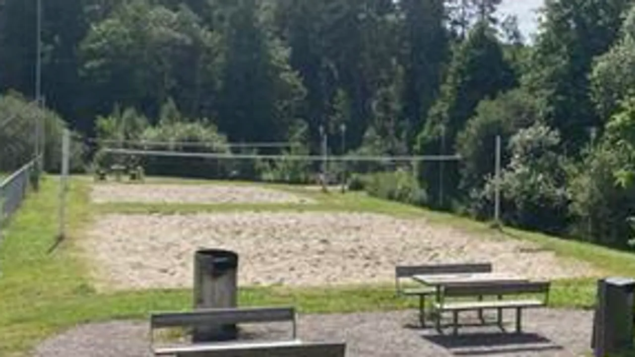 Et område med piknikbord og en sandvolleyballbane i bakgrunnen.