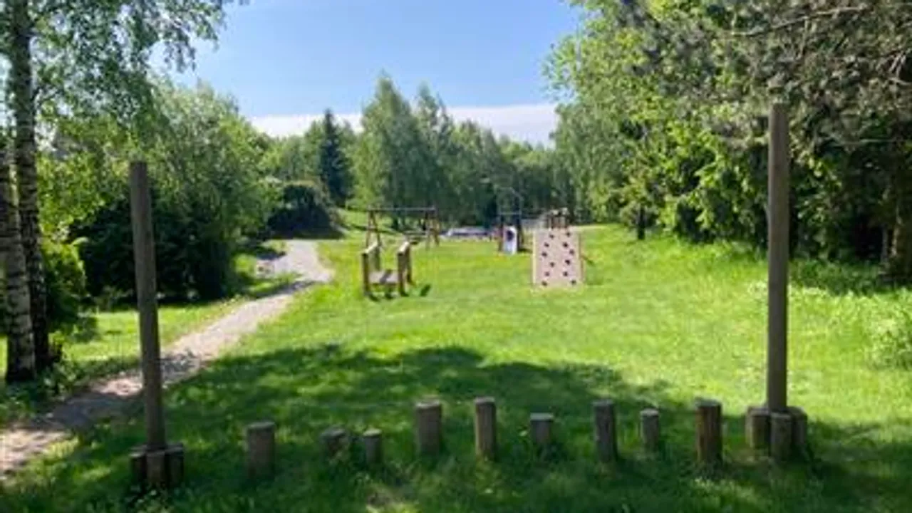 Et gressområde med flere trestolper i midten og en lekeplass.