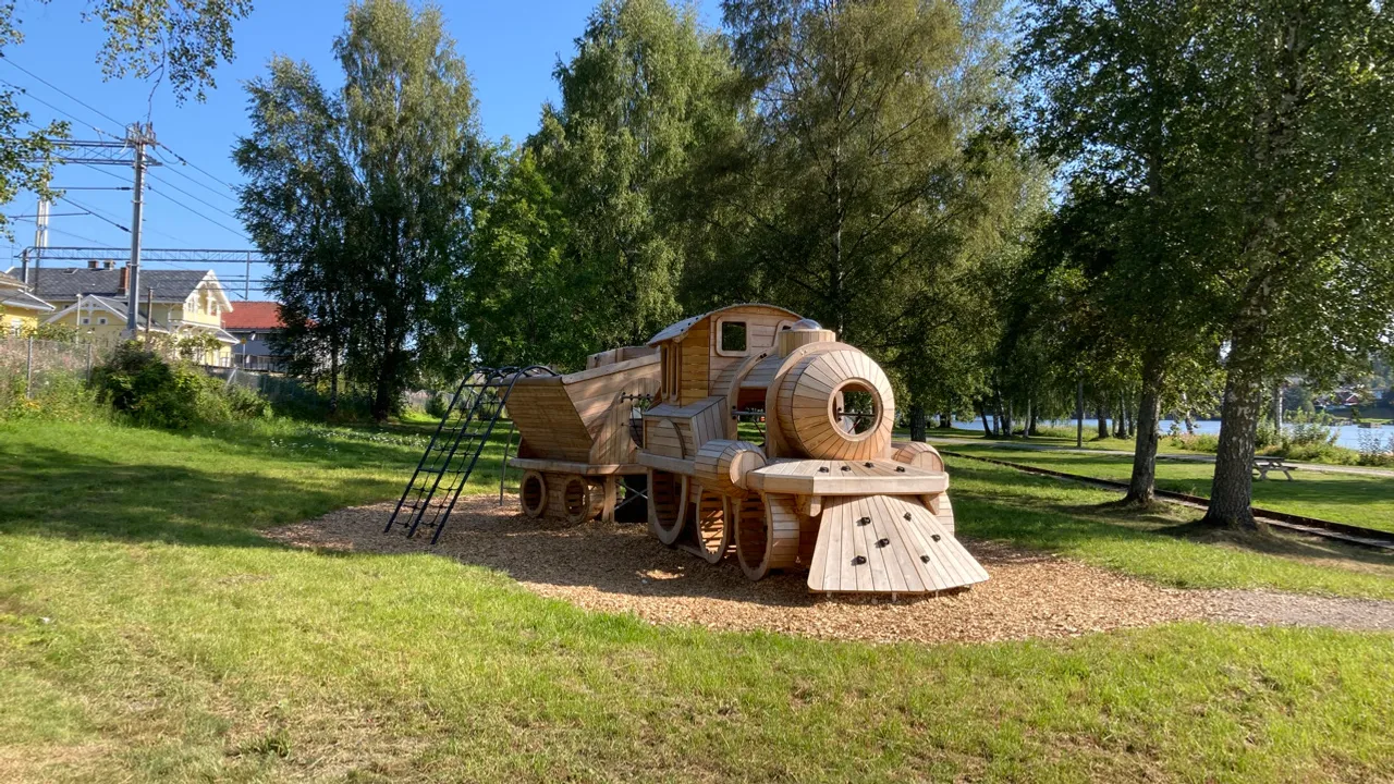 En lekestruktur som forestiller et tog laget av tre står midt i en park.